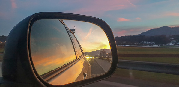 Red and orange colorful sunset viewed in Rear-view Mirror driving in nature.