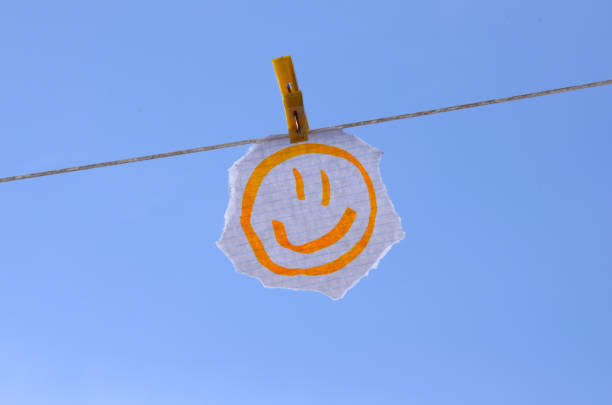 a drawn yellow smiley face on a piece of paper hanging on a clothespin, with the sky behind