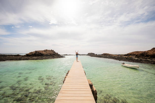 istock Ocean Bliss: Woman with Arms Raised on a Wooden Boardwalk 2000450284