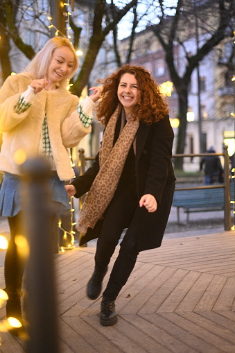 palyful redhead and blonde girlfriend women meet in park ,dance together in winter outdoors by night high res image