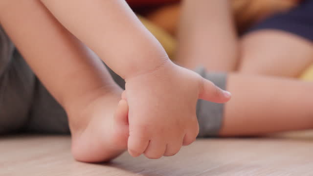 Close-up of foot small baby soft sole with hand playing during sitting on floor in living room at home. Tender foot of precious child Innocence. Love and Parenting concept.