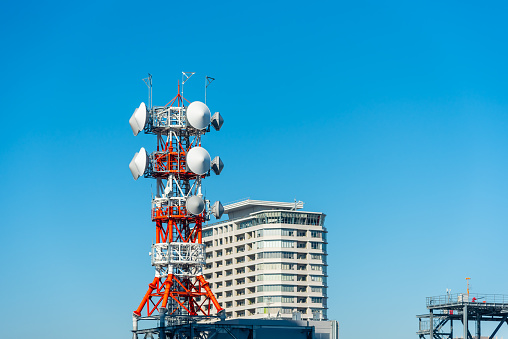 Telecommunication tower and broadcasting tower with satellite dish on top of building in blue sky.