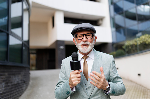 Senior man news reporter in live broadcasting. TV reporter presenting the news outdoors.