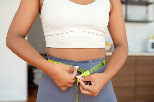 Cropped shot of fit woman measuring her toned waist with tape, following healthy nutrition and fitness routine, checking her slimming progress. Health and workout discipline, weight loss