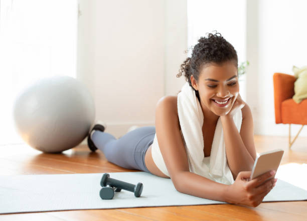 istock Sporty woman browsing through cellphone lying on yoga mat indoors 2000481138