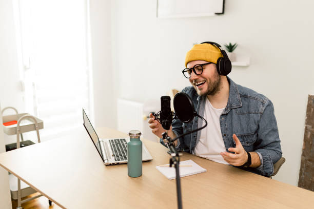 istock Young smiling man recording podcast and doing live streaming using microphone and headphones in recording studio 2000505024