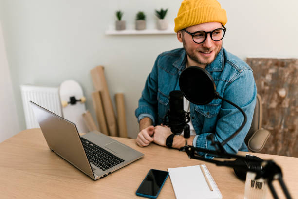 istock Young smiling man recording podcast and doing live streaming using microphone and headphones in recording studio 2000510454