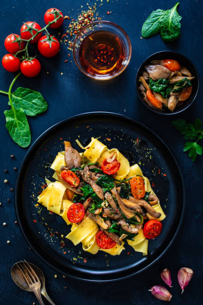 istock Noodles with oyster mushrooms with spinach and tomatoes on black table 2000517114