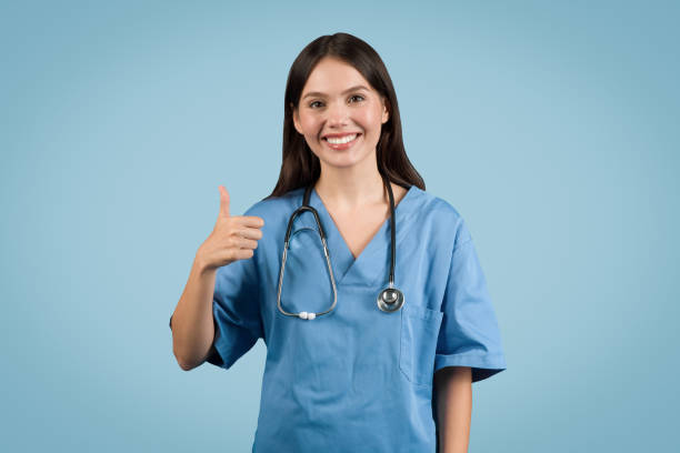 istock Smiling nurse in blue with stethoscope giving thumbs up, blue background 2000519793