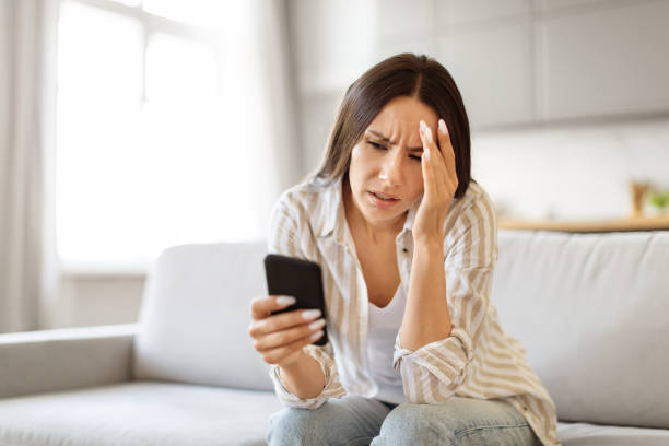istock Worried young woman looking at smartphone screen at home and touching head 2000547202