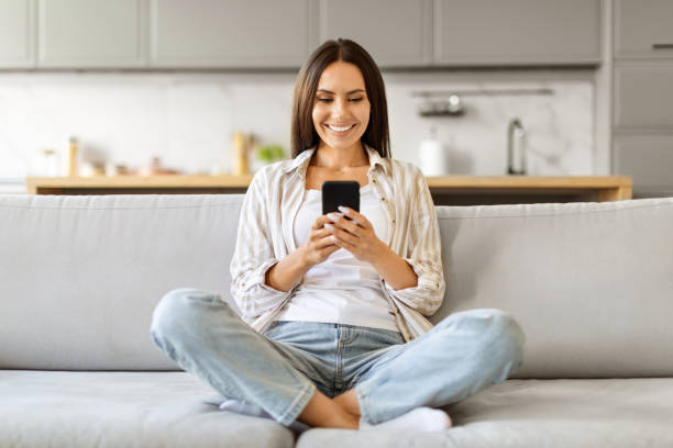 istock Young Smiling Woman With Smartphone Resting On Couch At Home 2000547211
