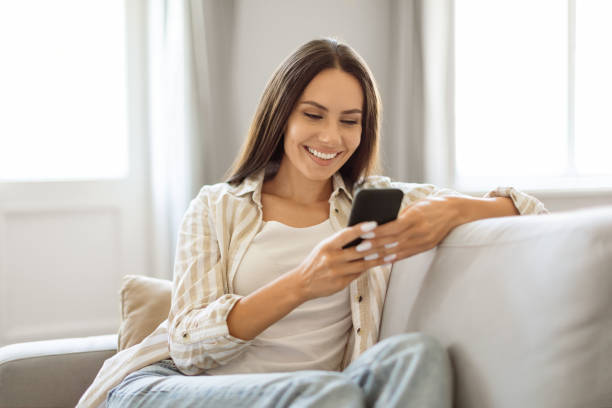 istock Relaxed young woman smiling and browsing her smartphone while reclining on couch 2000547213