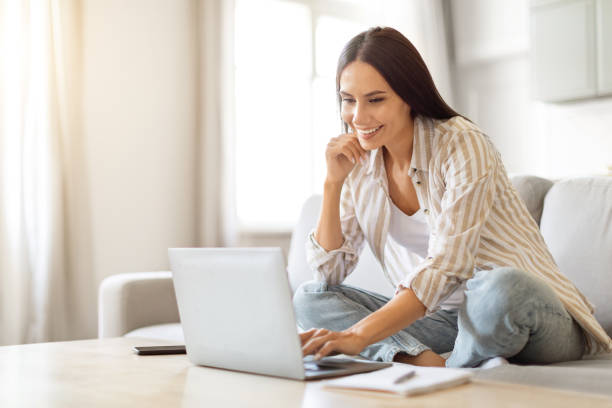 istock Smiling young woman using laptop for remote work at home 2000547225