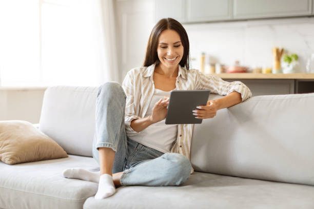 istock Young woman browsing internet on digital tablet while relaxing in living room 2000547740