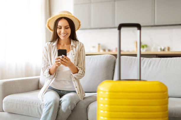 istock Smiling woman in straw hat texting on smartphone, sitting next to suitcase 2000547756