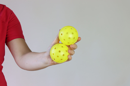 Woman athlete holding two yellow pickleball ball in the hands