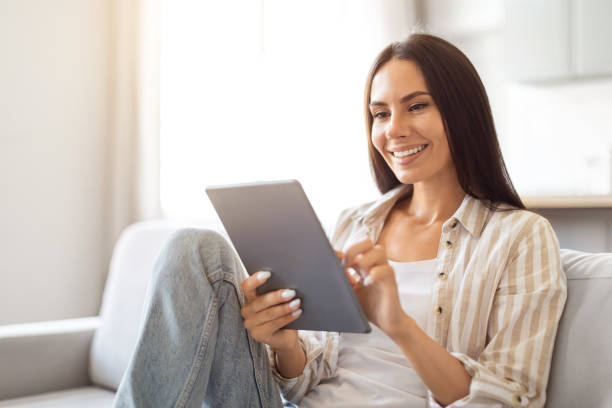 istock Great App. Happy Female With Digital Tablet Sitting On Couch At Home 2000547779