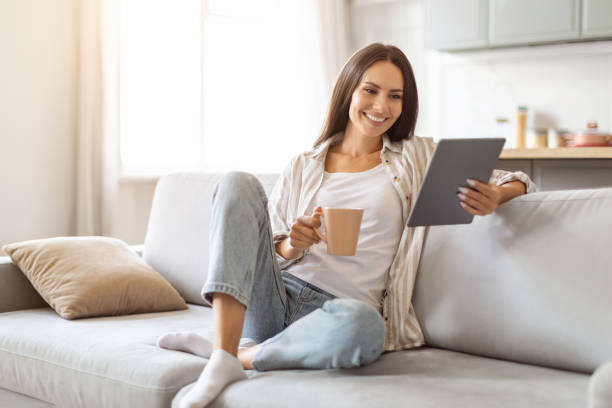 istock Smiling Young Woman Using Digital Tablet And Drinking Coffee At Home 2000548294