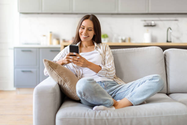 istock Happy Young Woman Messaging On Smartphone While Relaxing On Couch At Home 2000548358