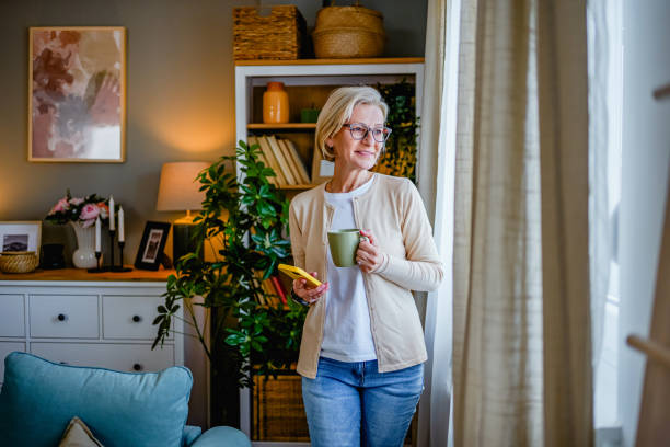 istock Woman with coffee looking through the window 2000555121