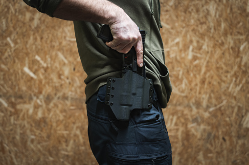 The man takes out a tactical pistol from his holster, close-up photo without a face. High quality photo