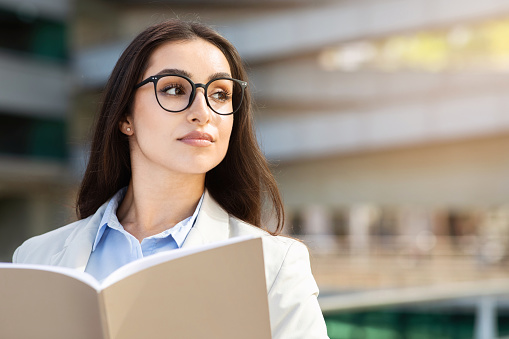 Serious pretty confident young woman in suit enjoy work, read book in city outdoors, look at free space, close up. Business, startup, study and lifestyle planning, ad and offer