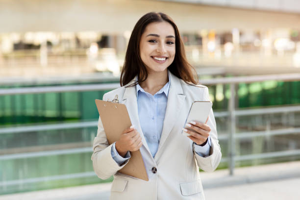 istock Efficient businesswoman multitasking with a clipboard and smartphone 2000563845