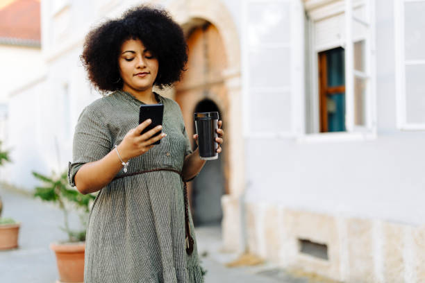 istock Beauty woman using her phone and drinking coffee on the street 2000564412