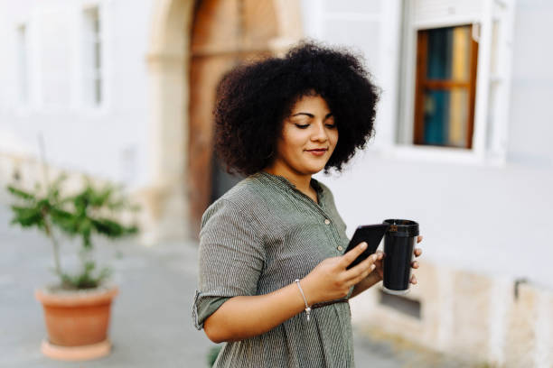 istock Beauty woman using her phone and drinking coffee on the street 2000564678