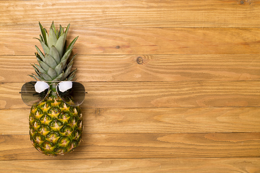 Creative pineapple hipster in sunglasses on wooden background, top view