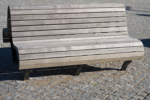 Gray wooden bench on gray paving stones.