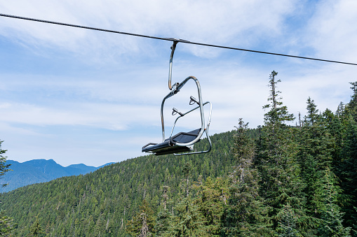 An empty chairlift chair elevated above a forest with lush mountains in the background.