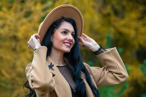 Outdoor portrait of a beautiful young brunette woman in a beige coat and hat