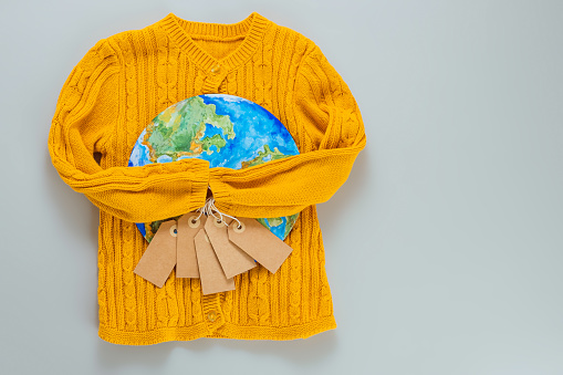 A yellow knitted sweater with a painted planet Earth on a gray background. Flat lay, top view