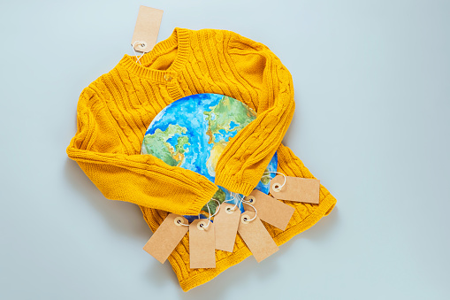 A yellow knitted sweater with a painted planet Earth on a gray background