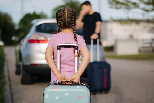 Dad and daughter are standing with their suitcases near a car with an open trunk. Happy little girl preparing to travel . High quality photo