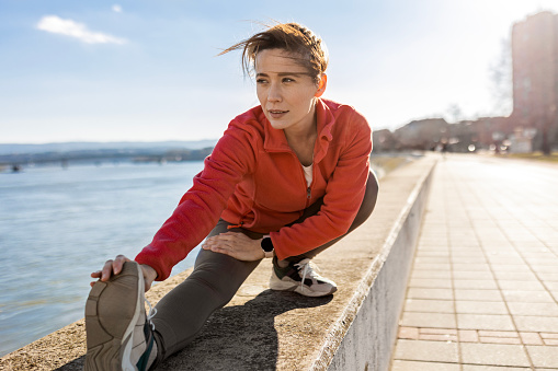 Happy sportswoman getting ready for jogging by stretching