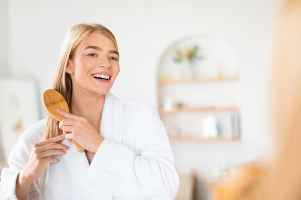 istock Young blonde lady in bathrobe brushing hair standing in bathroom 2000632263