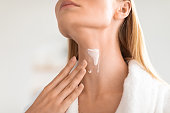 Cropped of blonde lady applying cream moisturizing her neck indoor