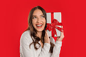Cheerful elegant lady holds wrapped gift box on red background