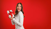 Young woman in dress holding gift box on red background