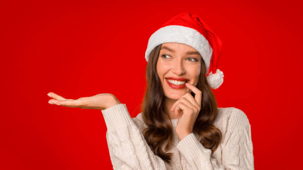 istock Cheerful young woman in Santa hat gesturing open hand, studio 2000639176
