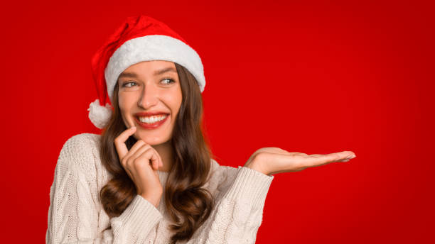 istock Lady in Santa hat gesturing showing open palm, red background 2000639181