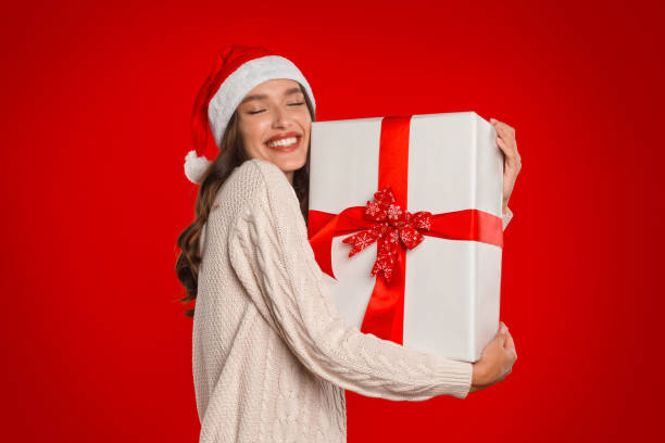 istock Happy lady holds Christmas gift standing on red studio background 2000639207