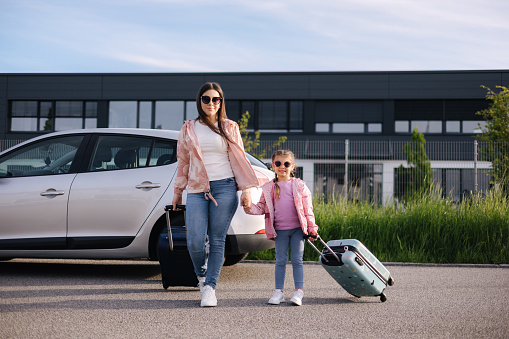 Adorable daughter with her mom go to airport with suitcases. Two girls goes to a trip. Little girl travel with mom. High quality photo