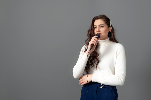 attractive female conference speaker during presentation, holds microphone and makes some gestures, isolated on gray