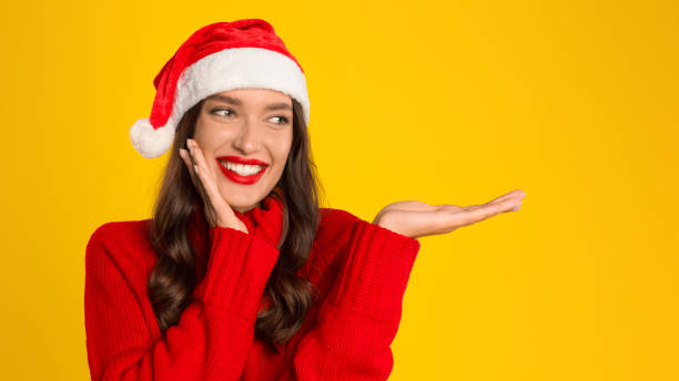 istock lady with open palm on yellow background, wearing Santa hat 2000654460