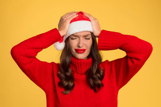 istock woman in Santa hat suffering with headache against yellow backdrop 2000654470