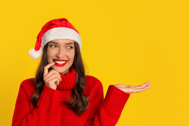 istock woman in Santa hat extends hand to present product, studio 2000654755