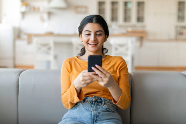 istock Beautiful young indian woman using her smartphone while sitting on couch 2000663538